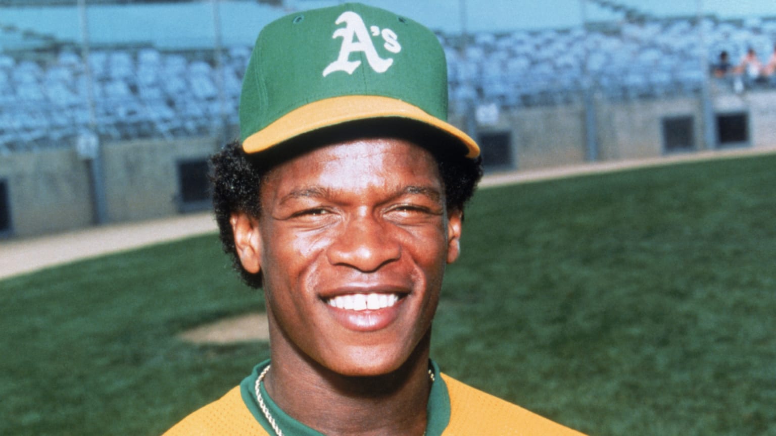 A smiling Rickey Henderson wearing the green and gold of the Oakland A's
