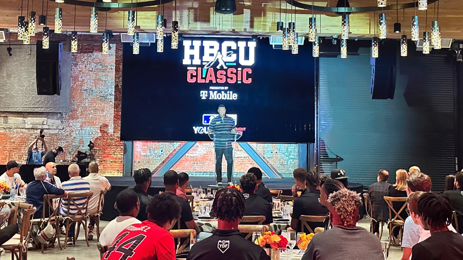 A wide view of people at a banquet listening to a speaker on stage