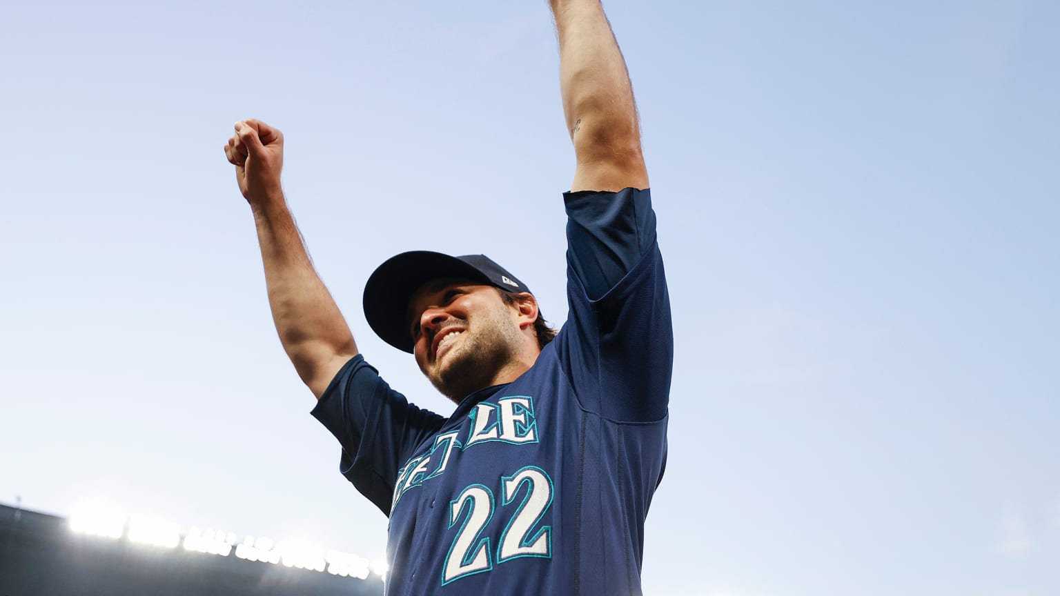 Luis Torrens, in a blue Mariners jersey, smiles and raises his arms to the sky celebrating a victory