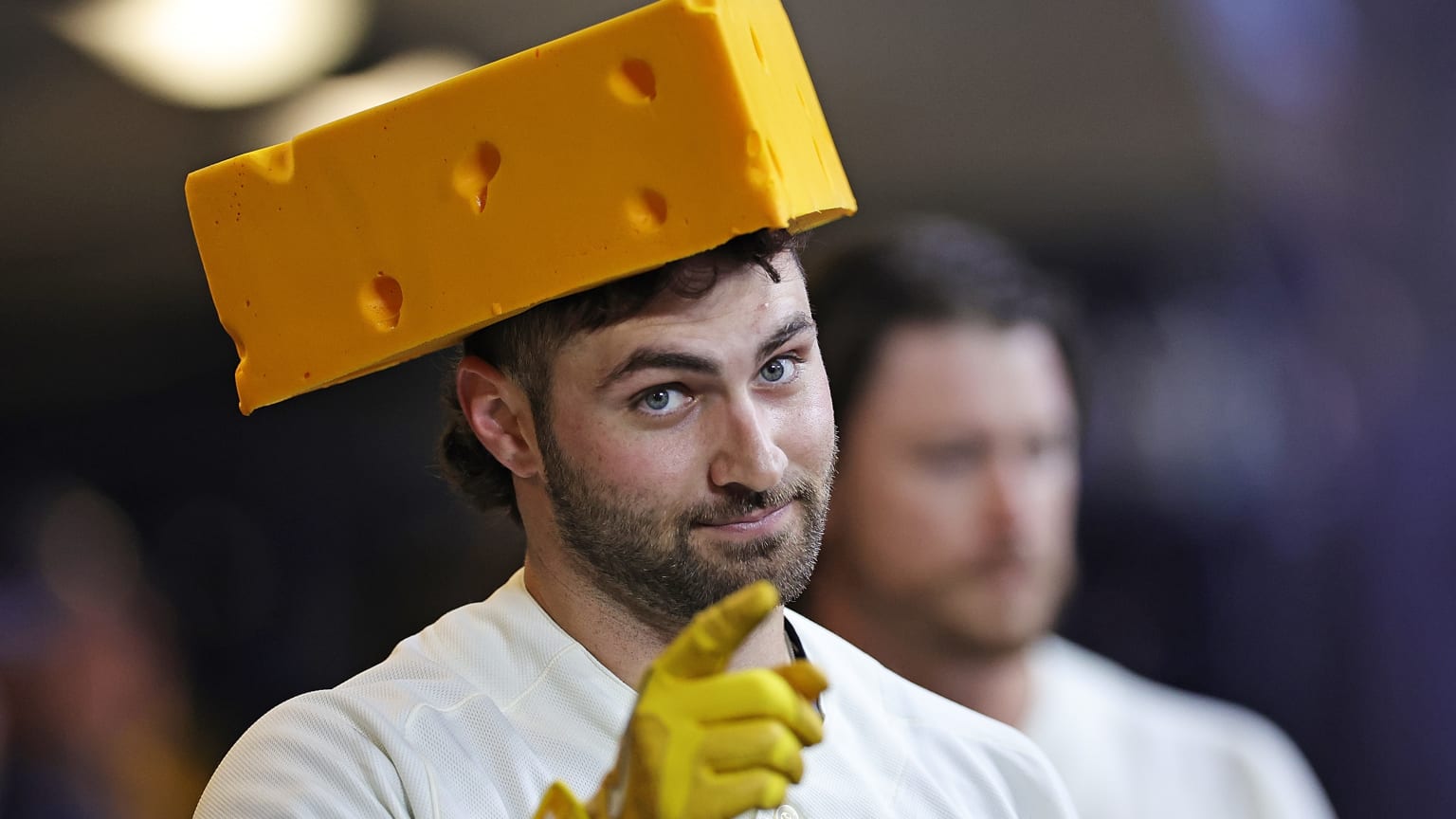 Garrett Mitchell points at the camera wearing a cheesehead hat