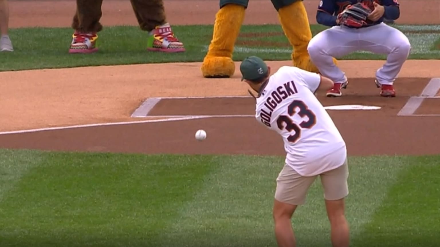 A man in a Twins jersey reading Goligoski above the number 33 sends a ceremonial first pitch toward the catcher with a hockey stick