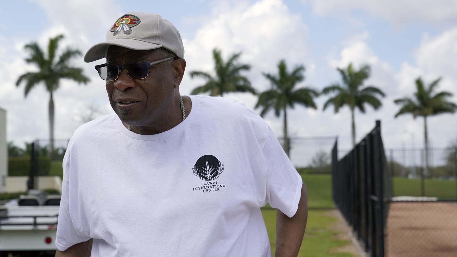 Dusty Baker in a white T-shirt, sunglasses and a beige cap in front of some palm trees