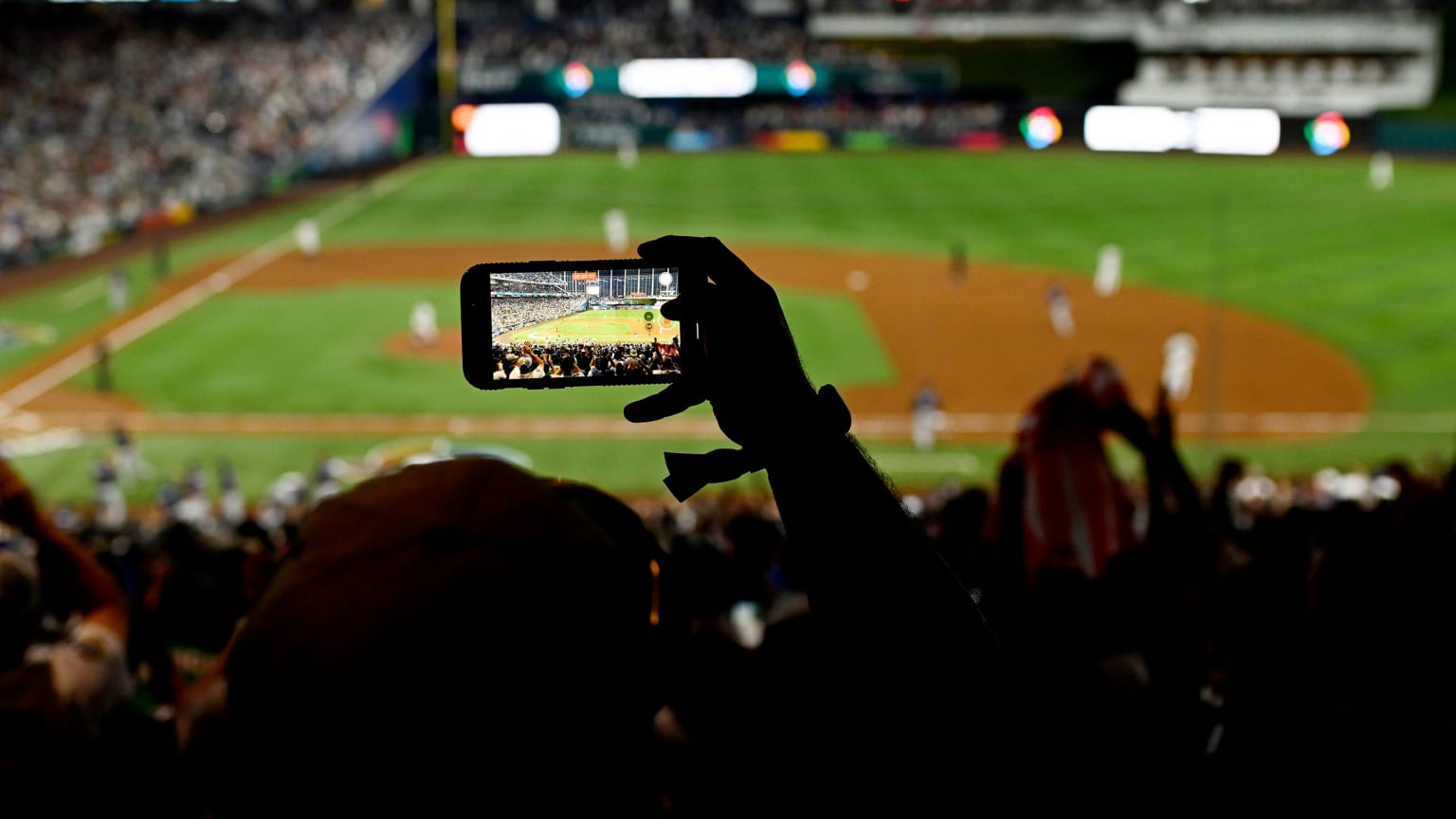 A fan holds up a cell phone to take a picture of a baseball field