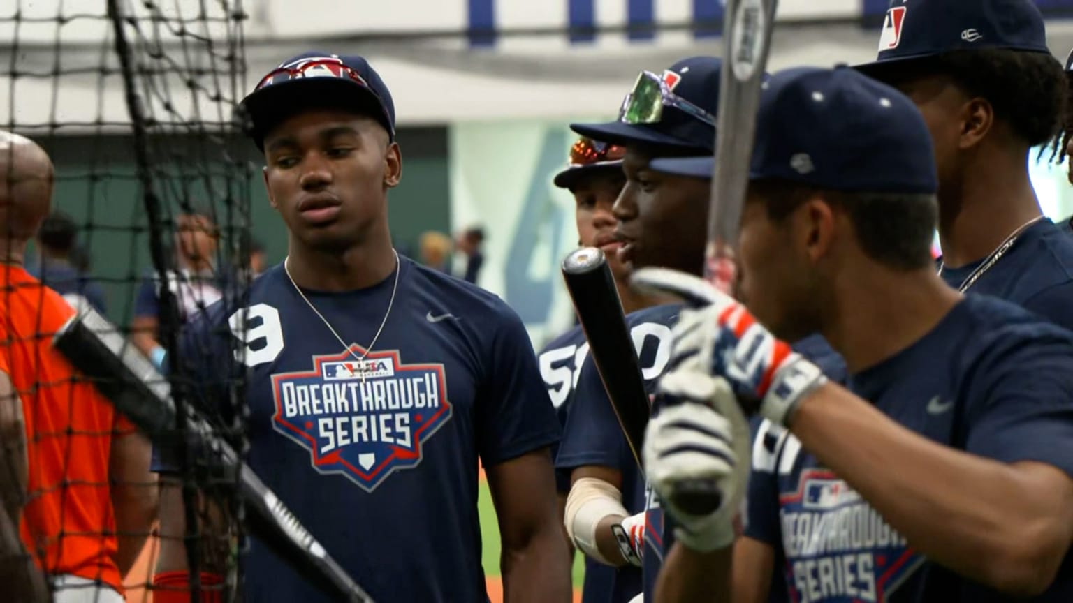 A group of younger baseball players wearing Breakthrough Series T-shirts gather in a group while holding baseball bats