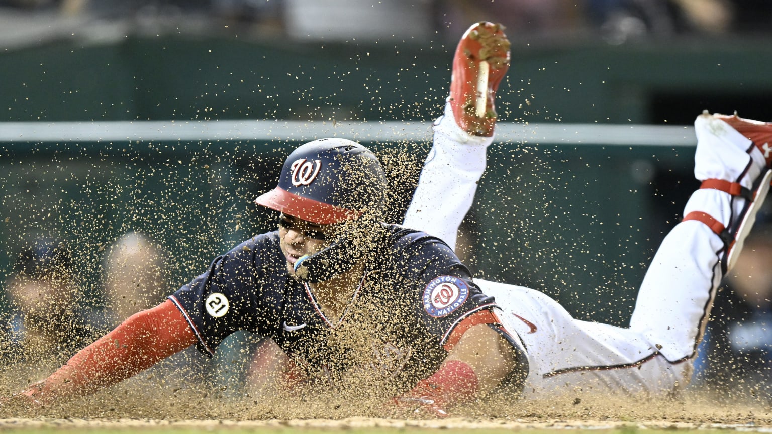 A player sliding head-first into home plate, dirt flying up around him