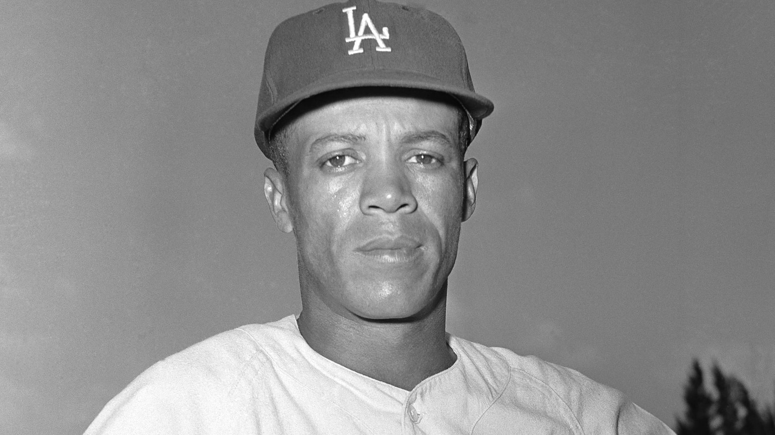 A black-and-white portrait of Maury Wills wearing an LA Dodgers cap