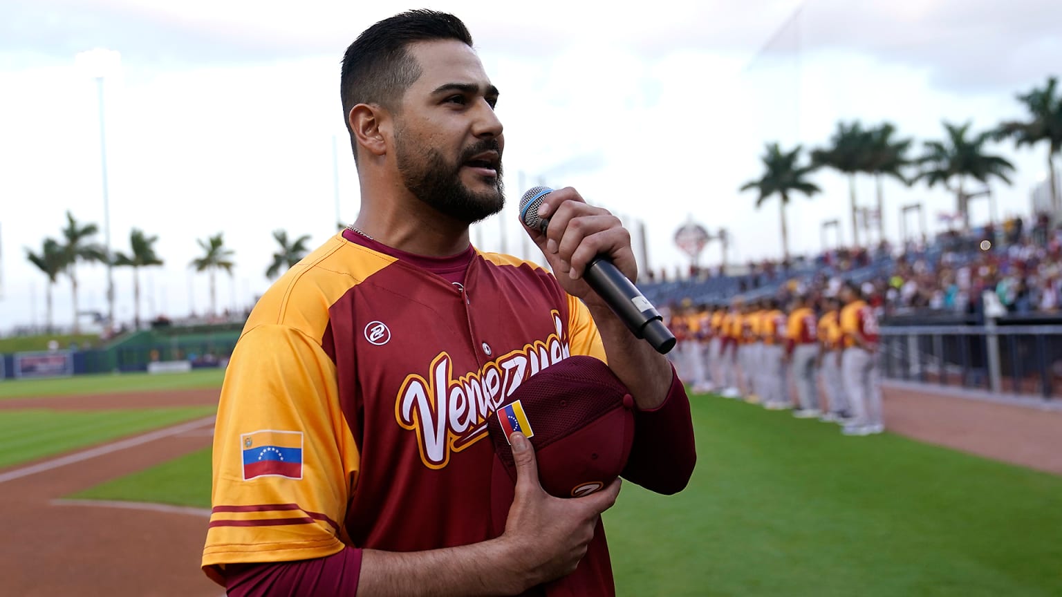 A player in a Venezuela jersey holds his cap over his heart while singing into a microphone
