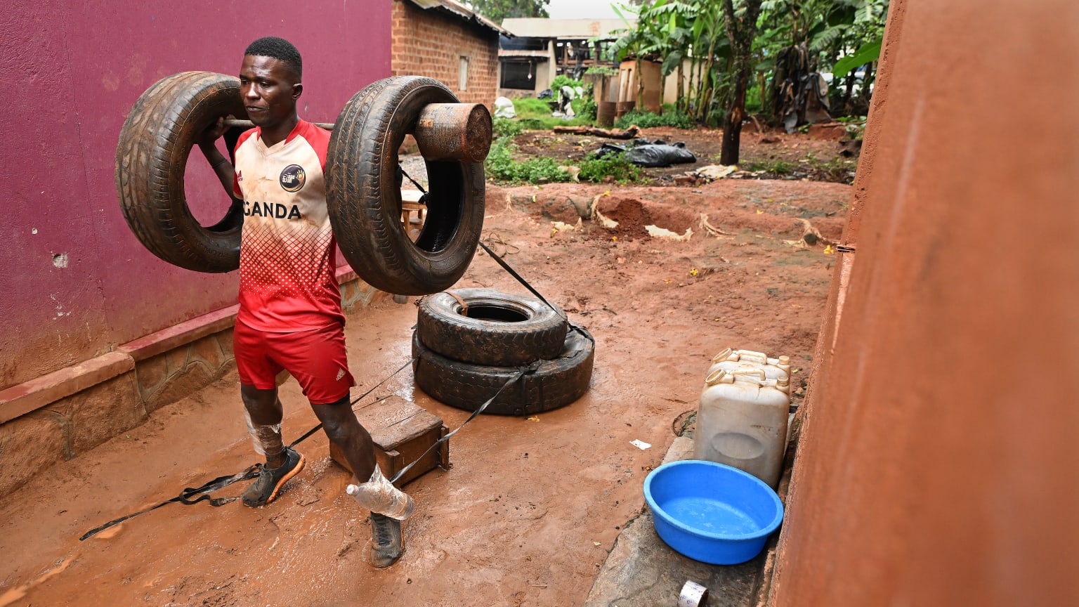 A young man works out in a muddy alley with two tires draped over a bar resting across his shoulders