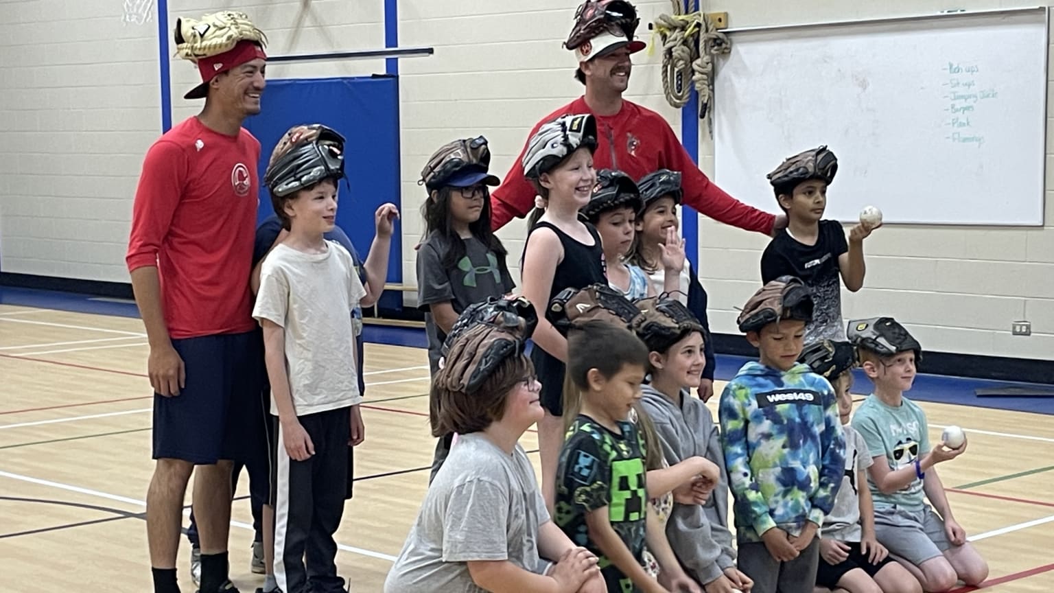 Two players pose with kids, all of them wearing gloves on their heads