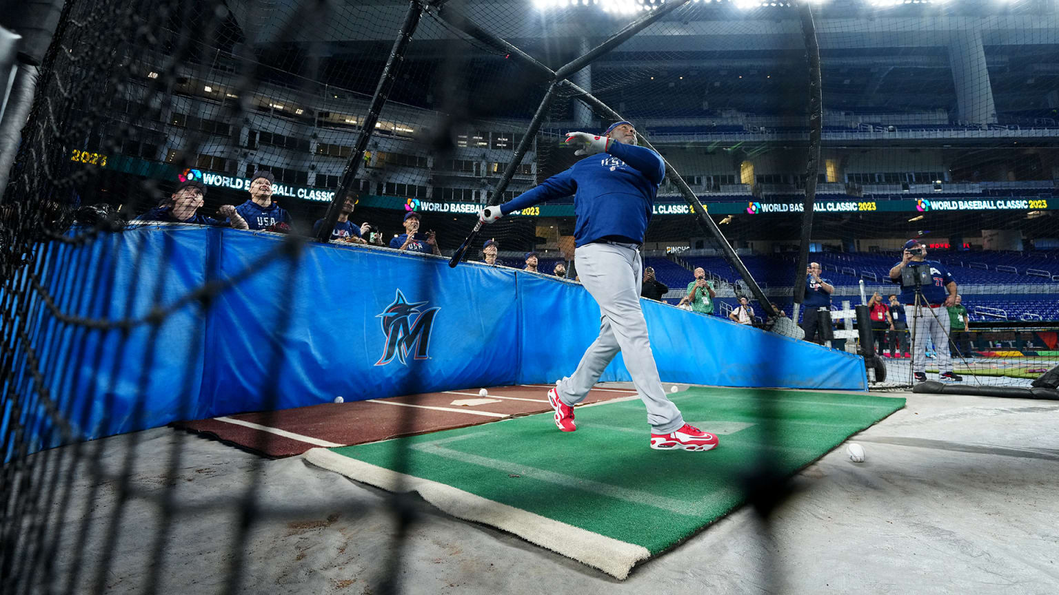 A view through a net at a player following through on a swing in the batting cage