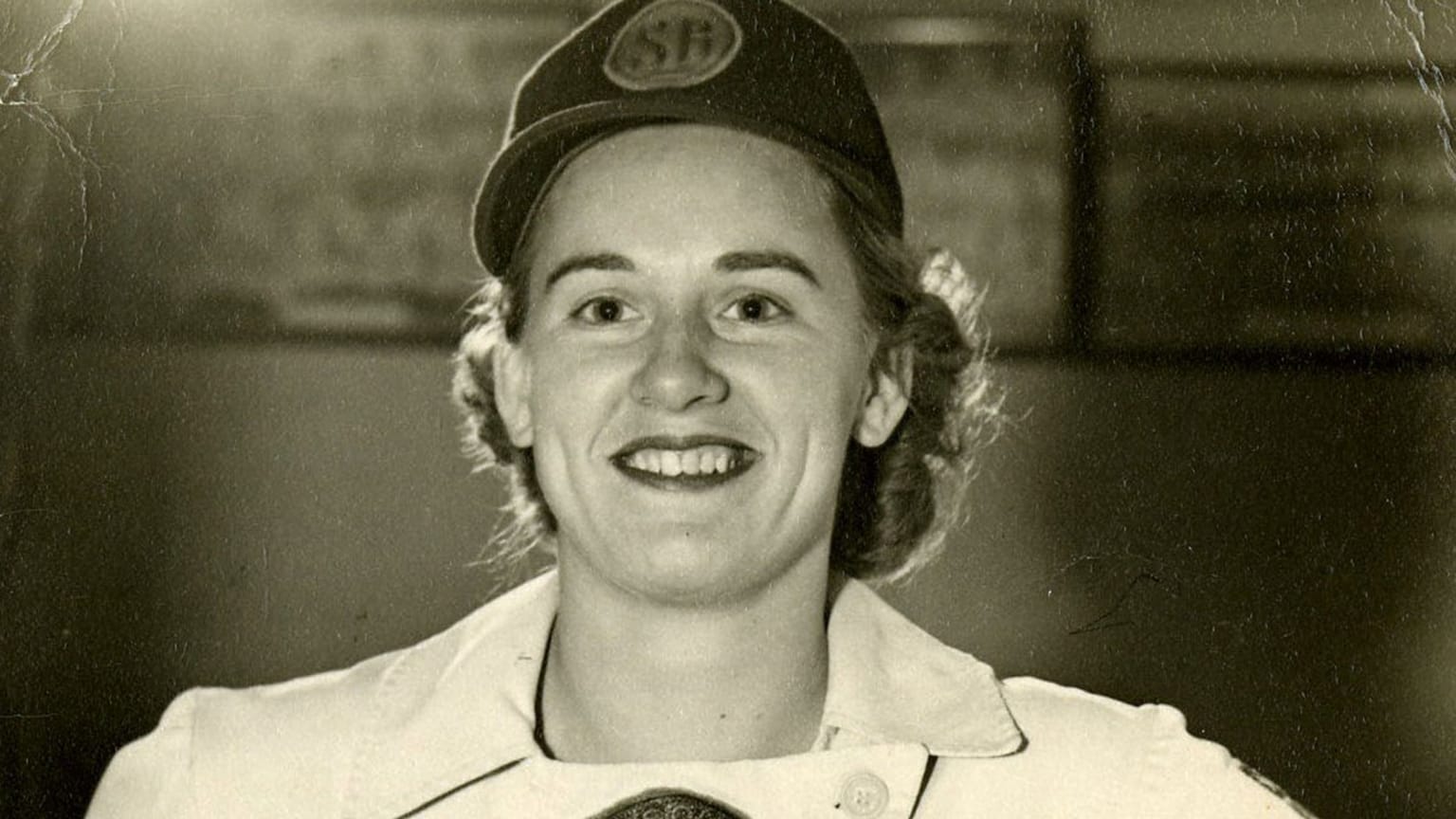 A black-and-white photo of a smiling woman in a baseball uniform