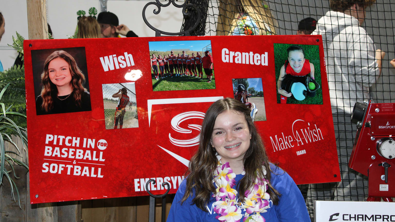 A young girl stands in front of a posterboard consisting of photographs and ''Wish Granted'' text at the top