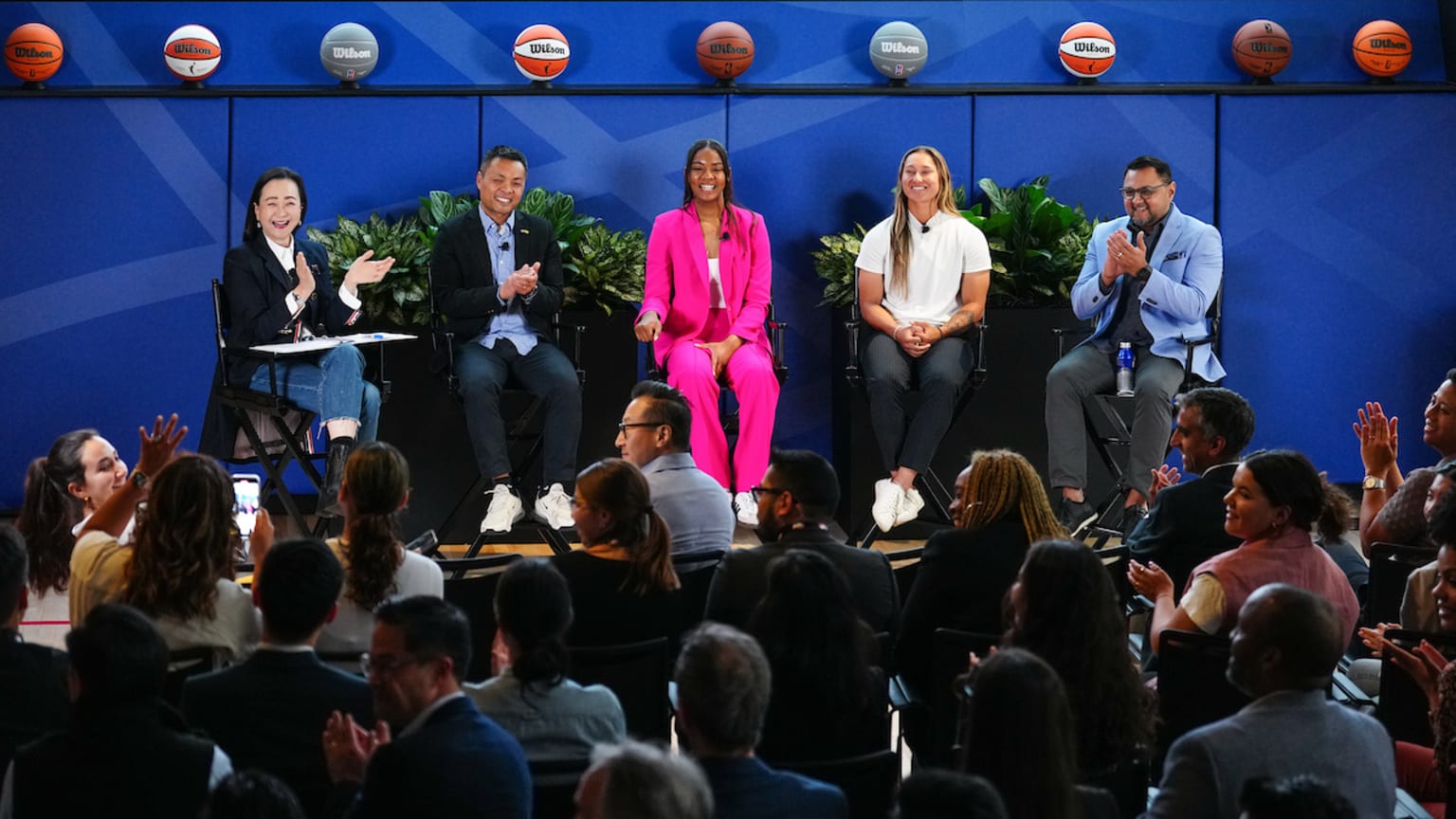 Five people sit on a stage in front of an audience