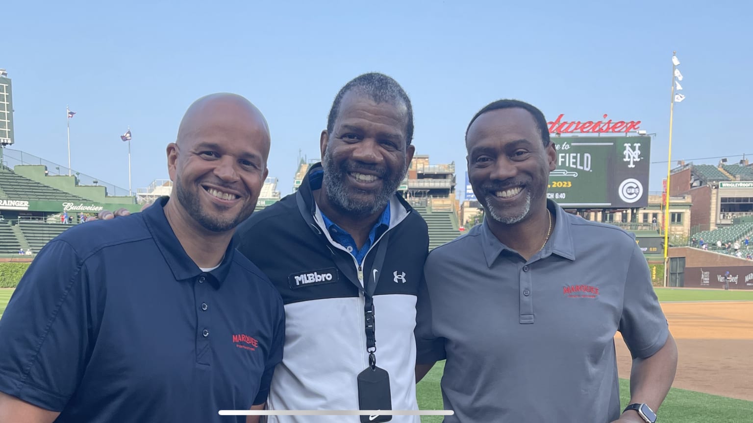 Three friends pose for a photo on a baseball field