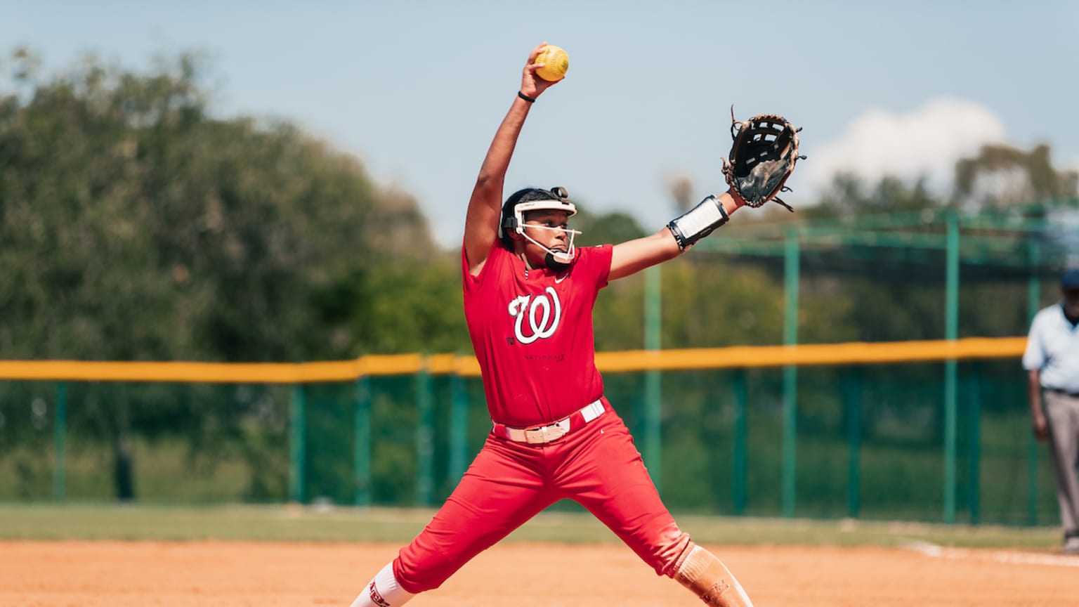 A softball pitcher in a red uniform with the Nationals logo on the jersey