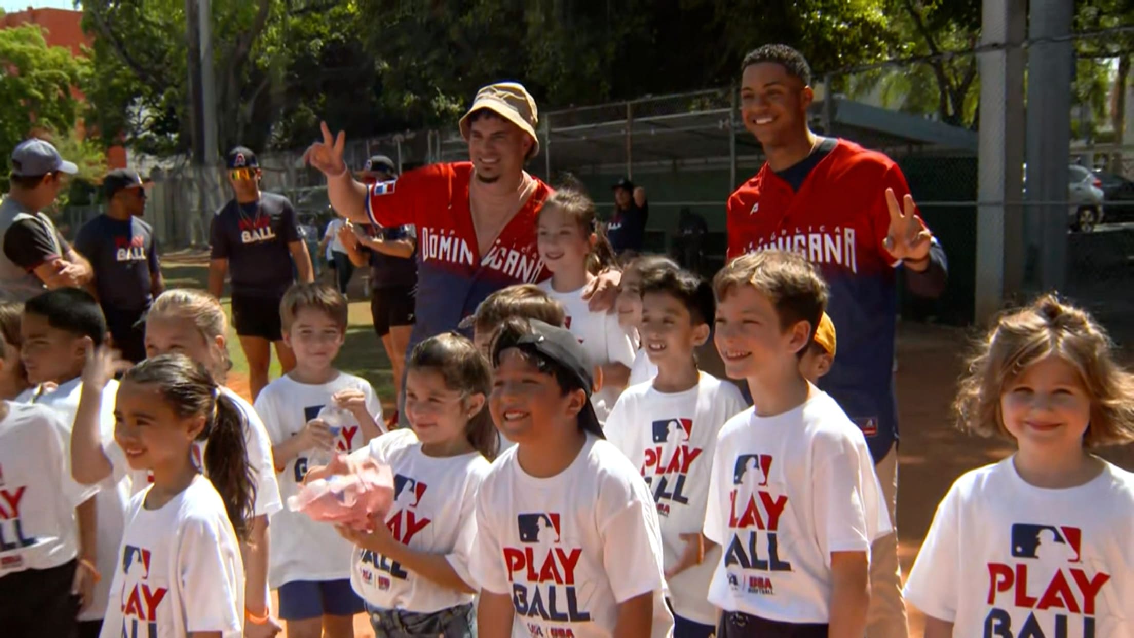 A screenshot of two players in red Dominican jerseys behind a group of kids in white T-shirts