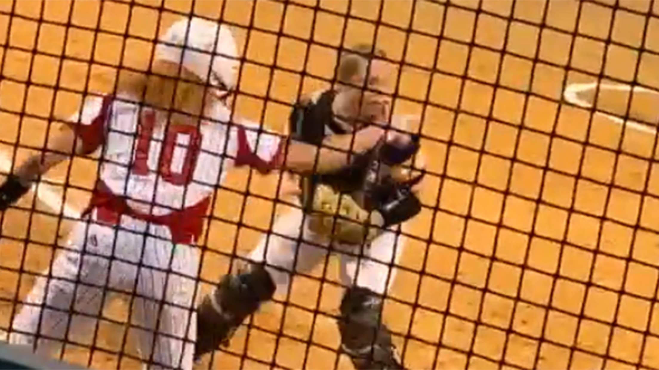 A video screengrab looking through a fence of a player wearing No. 10 pointing and the opposing catcher looking in that direction