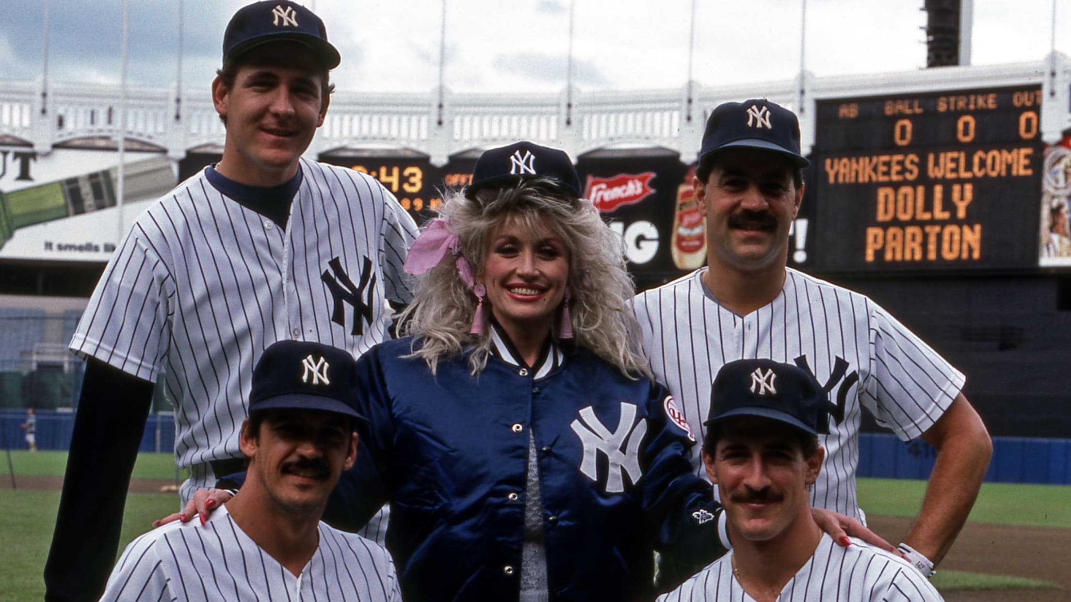 Dolly Parton in a Yankees cap and jacket along with four players