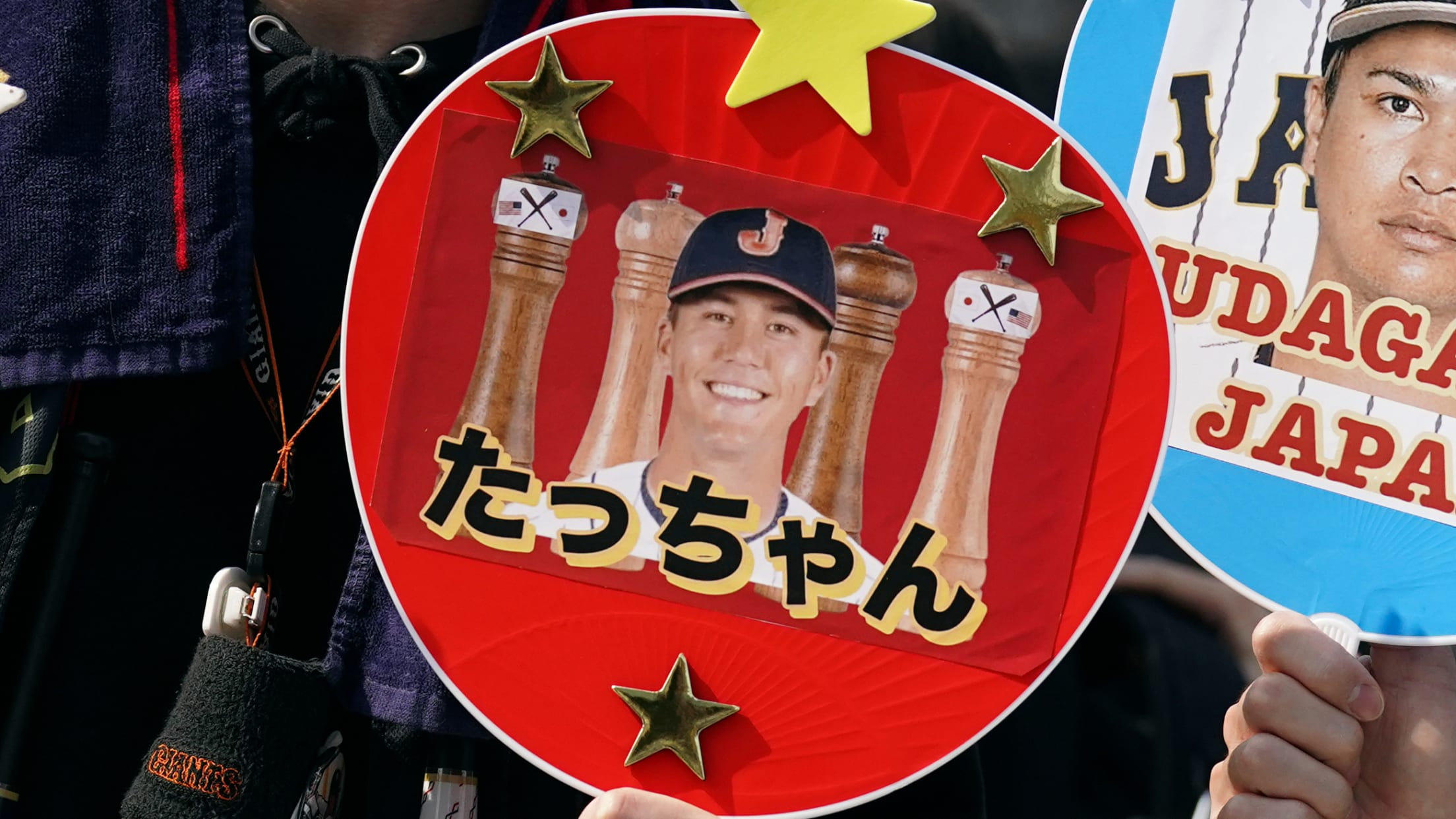 A red paddle fan showing a smiling player with a J on his cap and Japanese lettering underneath