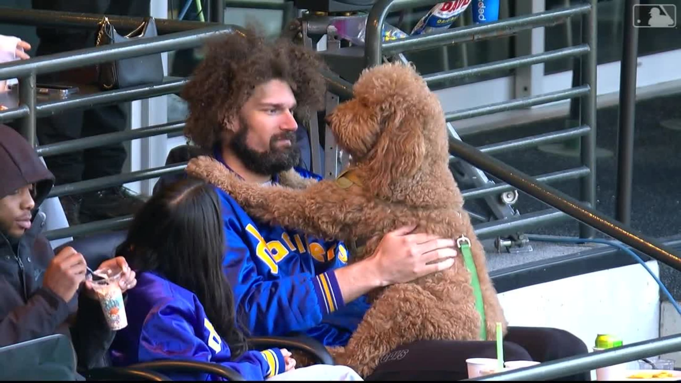 NBA player Robin Lopez looks into the eyes of a goldendoodle sitting on his lap at a ballgame