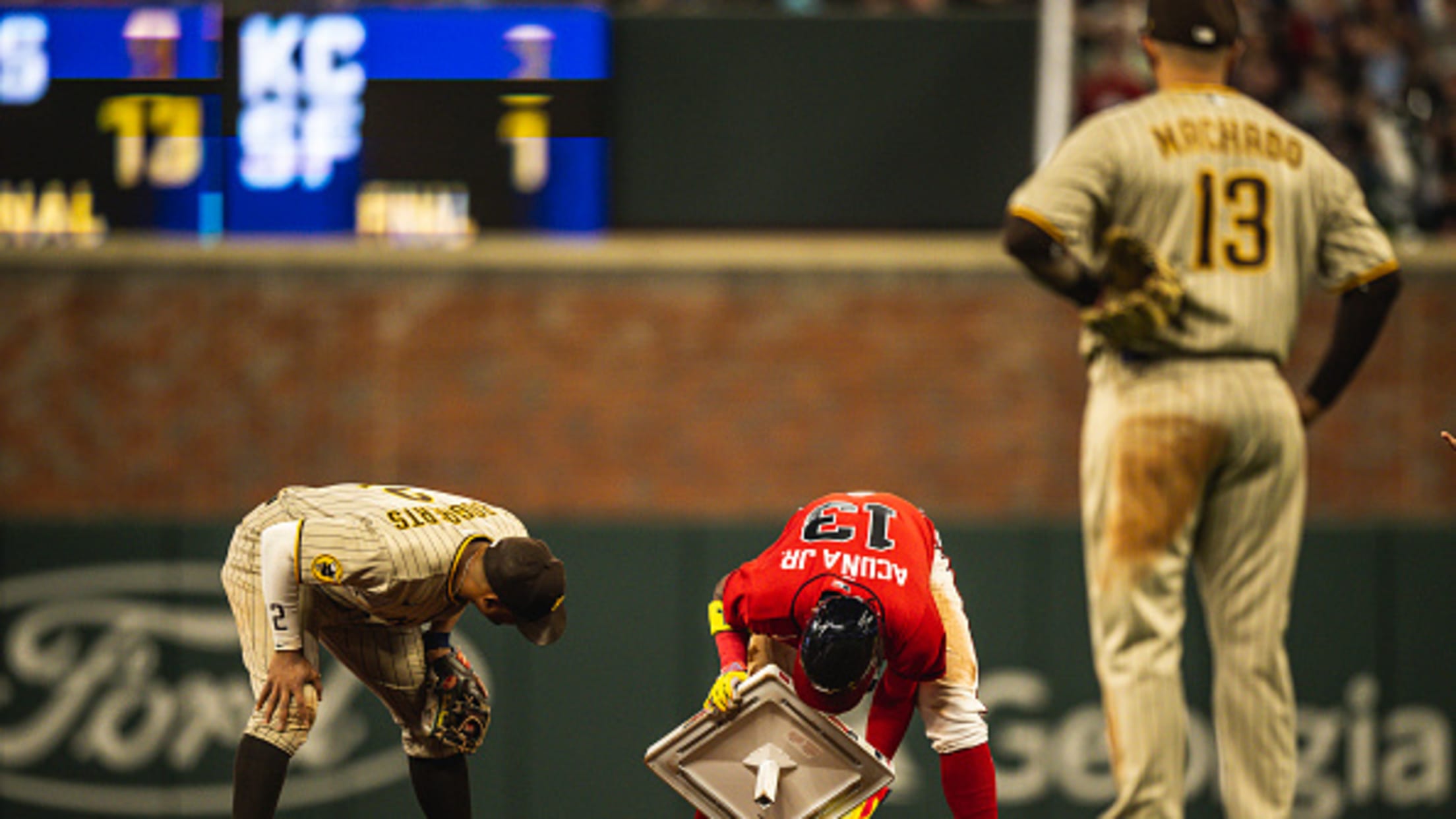 Two Padres watch as Ronald Acuña Jr. tries to put a base back into the ground