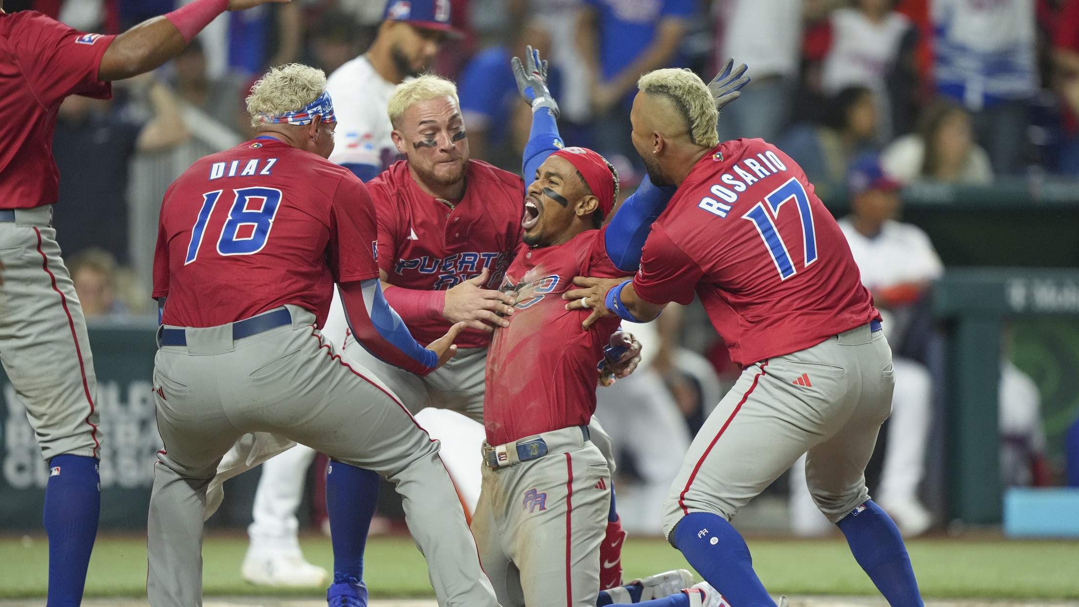 Francisco Lindor, on his knees, raises his arms in celebration as other Puerto Rican players surround him