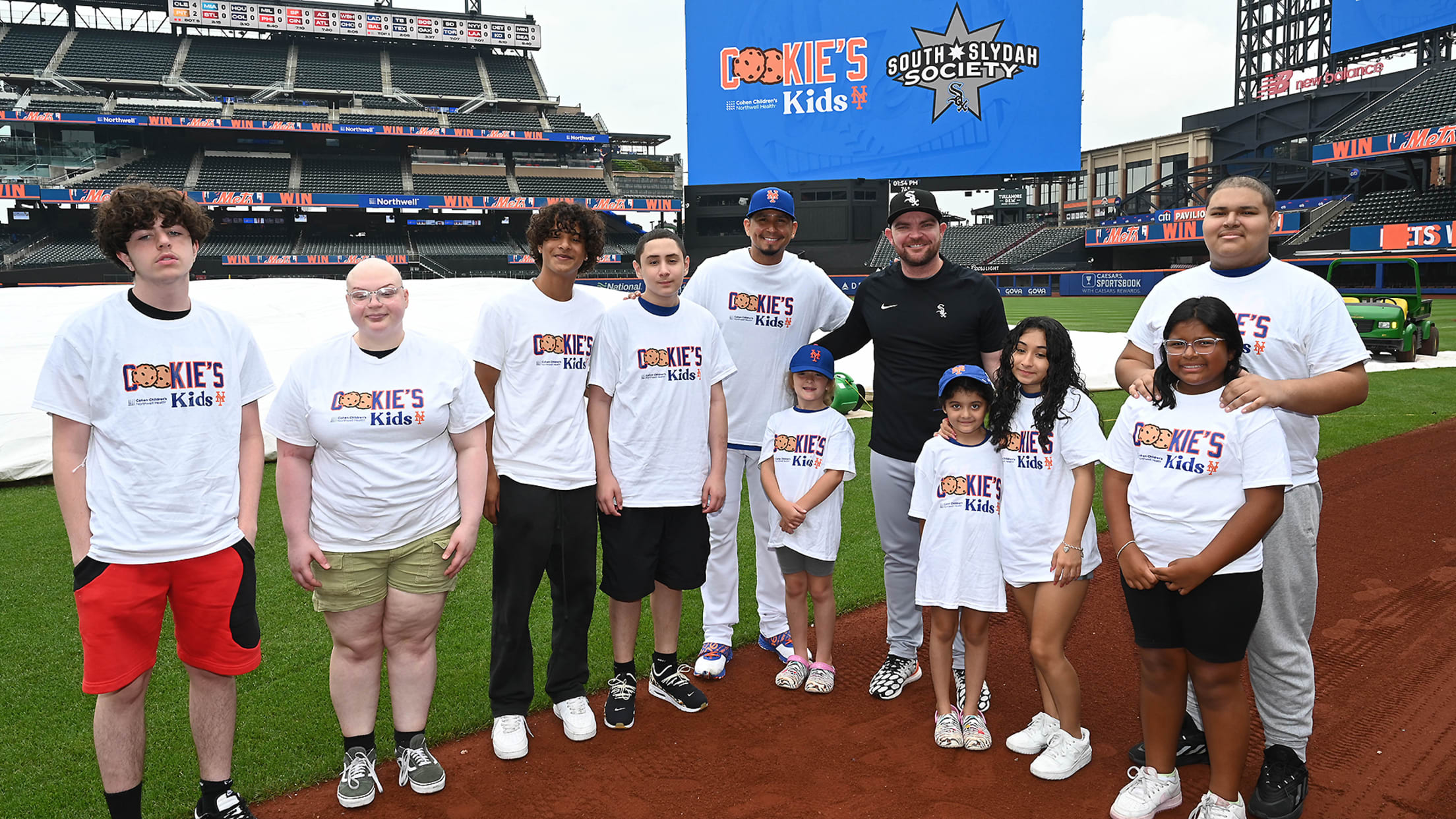 Several children stand on the field with the Mets' Carlos Carrasco and the White Sox' Liam Hendriks