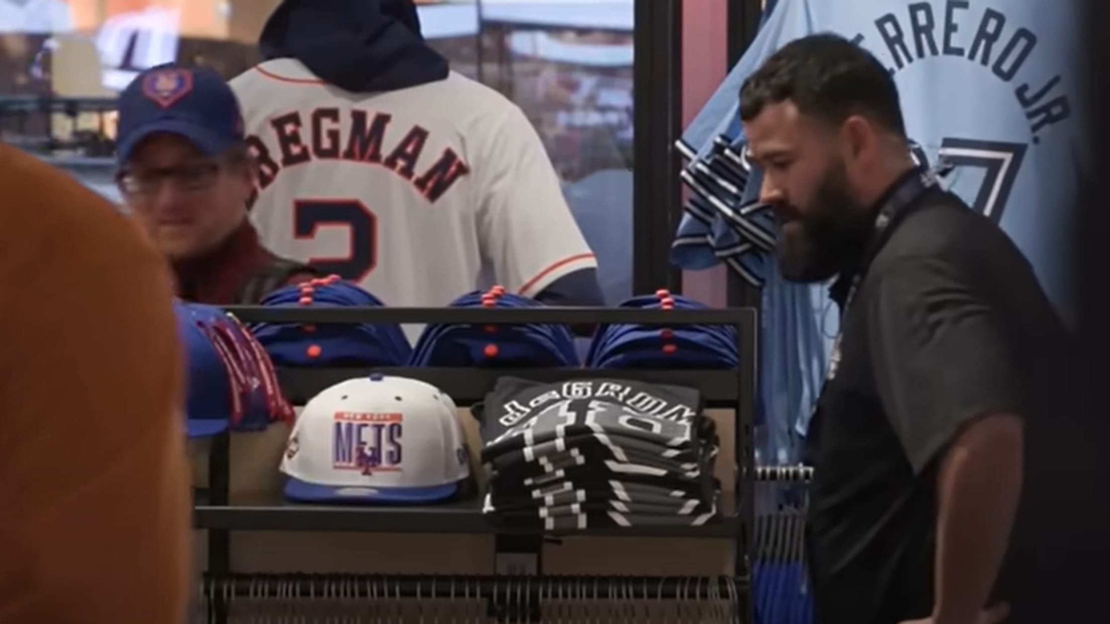 Two men in a store featuring MLB jerseys, caps and shirts