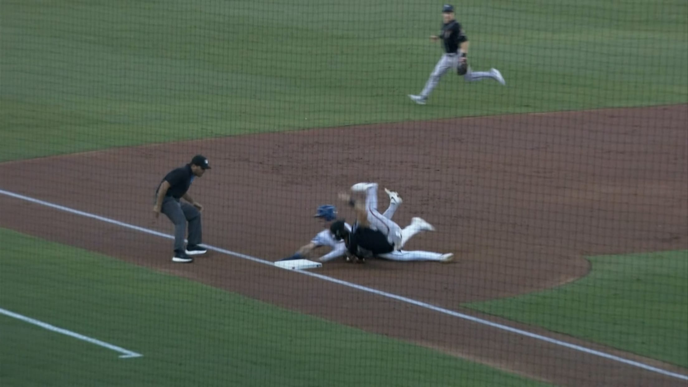 A screengrab of a third baseman tumbling onto his back as a runner slides into the base
