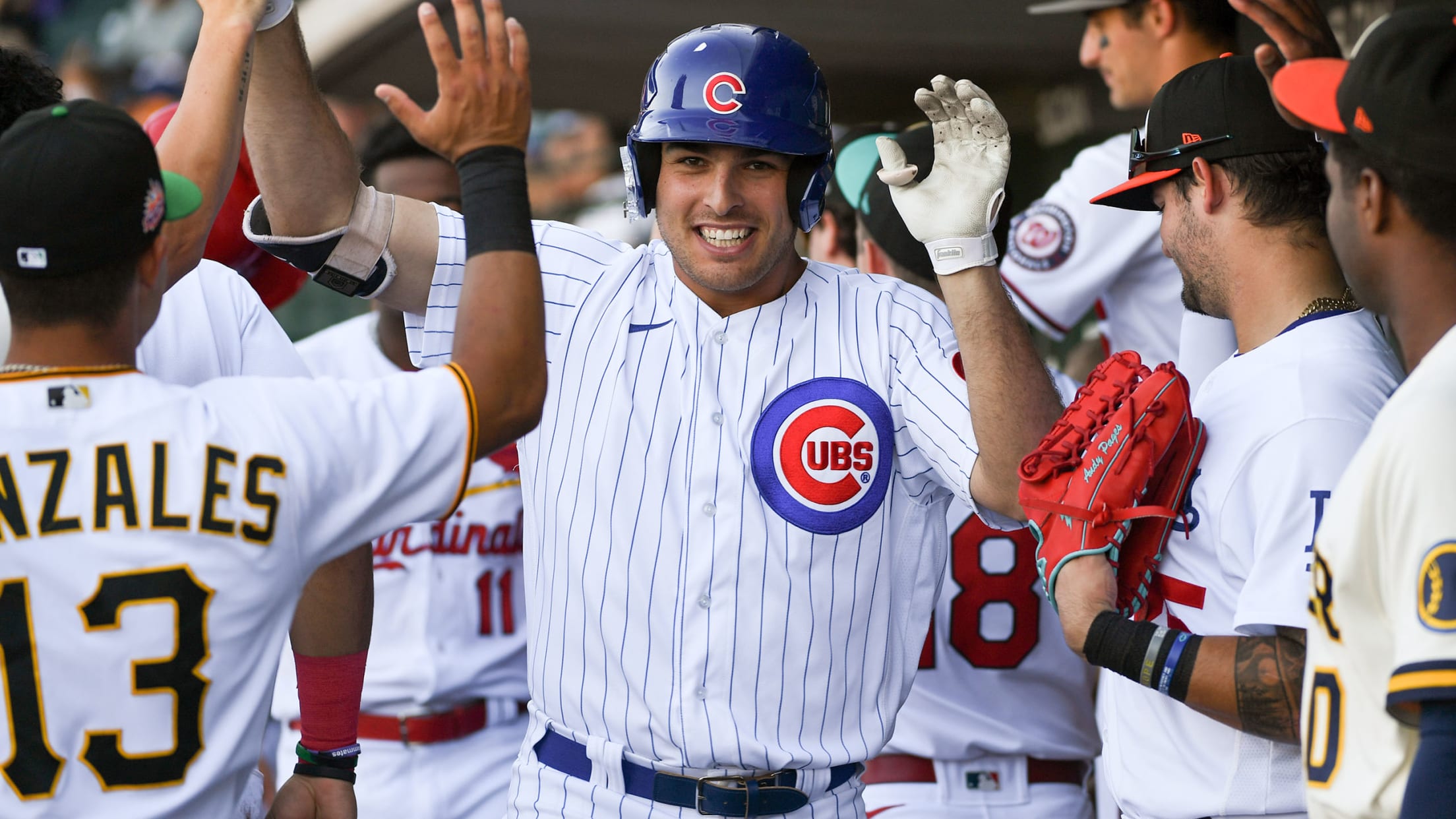 A player in a Cubs uniform gets high-fives in the dugout from players in other uniforms