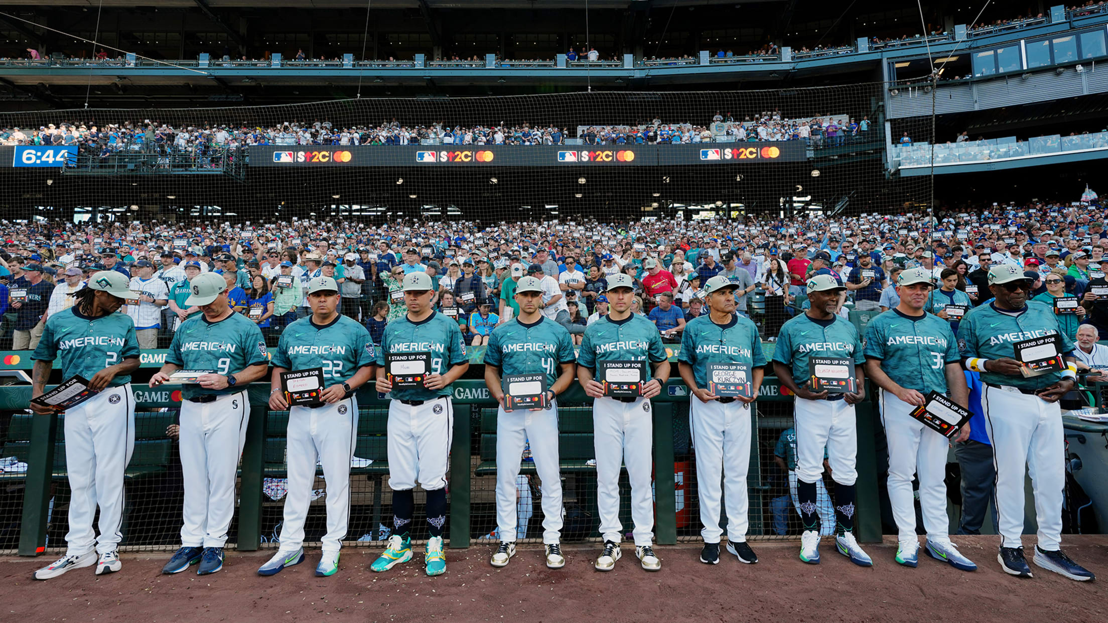 American League players line up in front of their dugout holding signs with loved ones' names on them