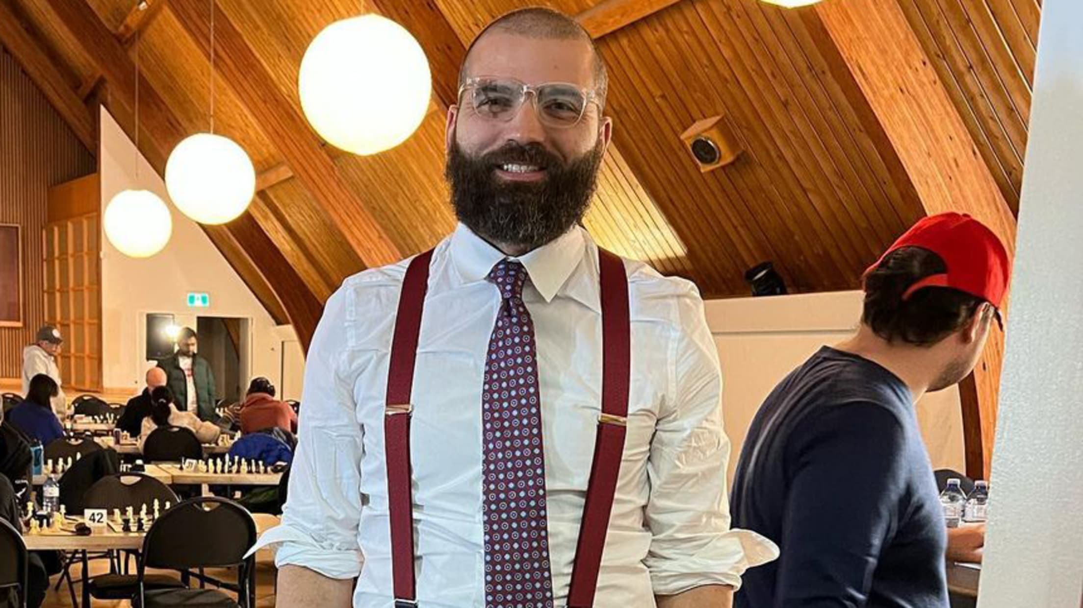 A bearded Joey Votto in wire-rimmed glasses, wearing a tie and suspenders