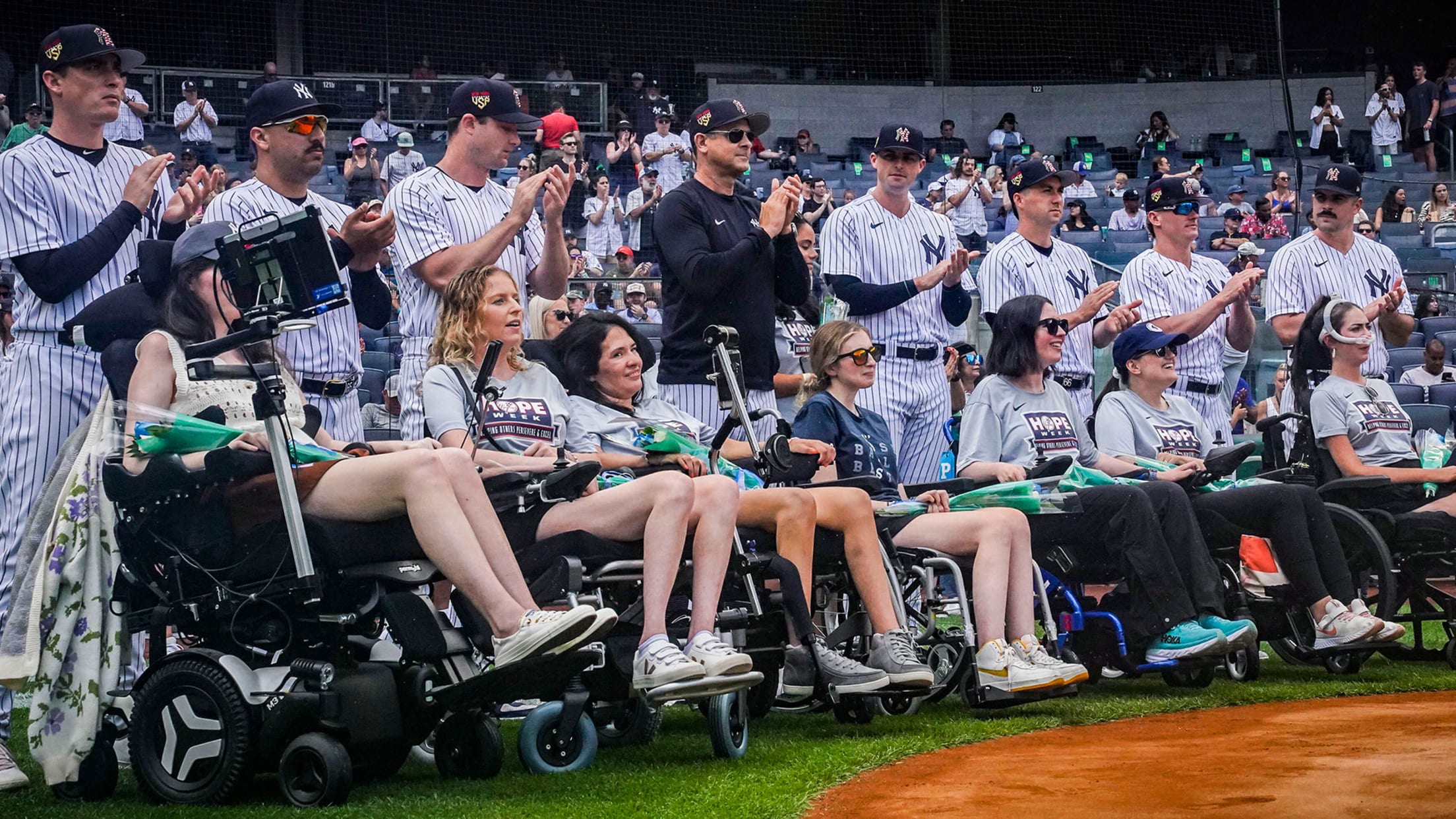 Several women in wheelchairs are joined by the Yankees on the field before the game