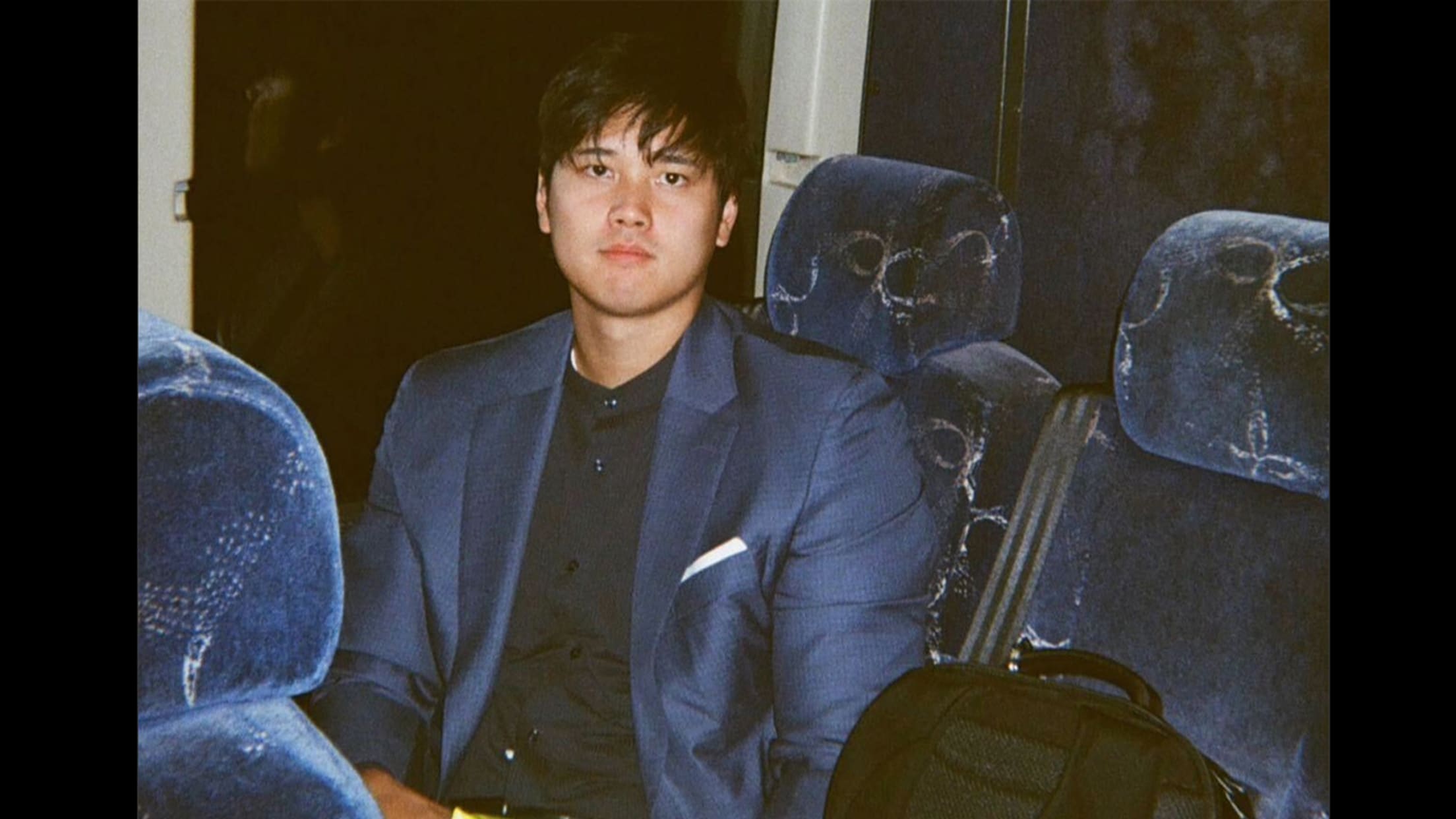 Shohei Ohtani sits on a bus and stares expressionless at the camera