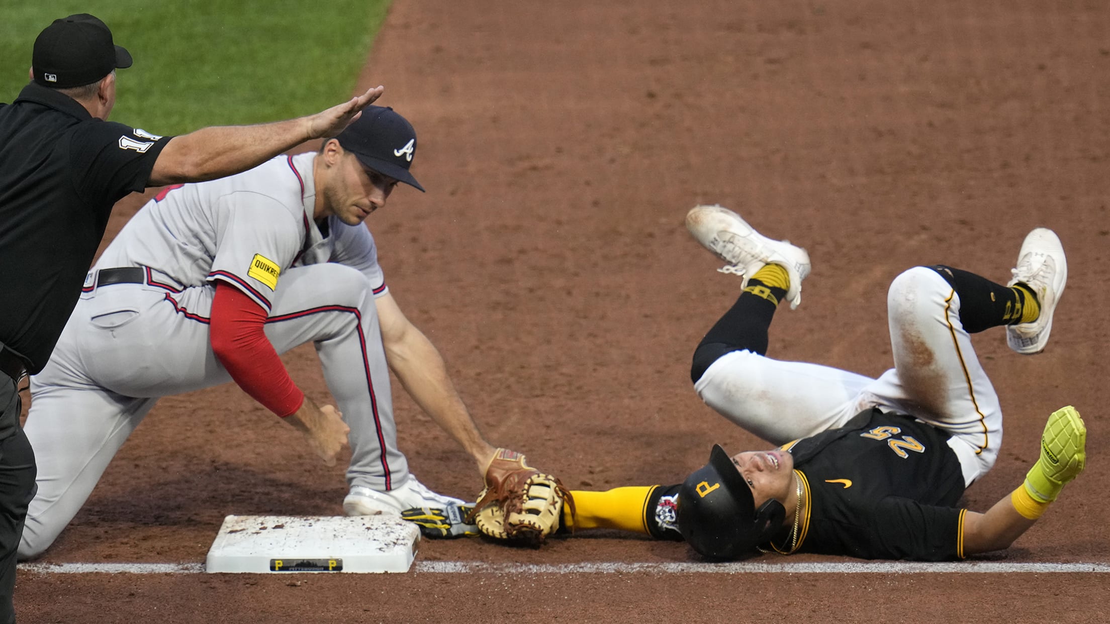 An umpire signals safe as Atlanta's first baseman holds the tag on the arm of a Pirates player lying on his back