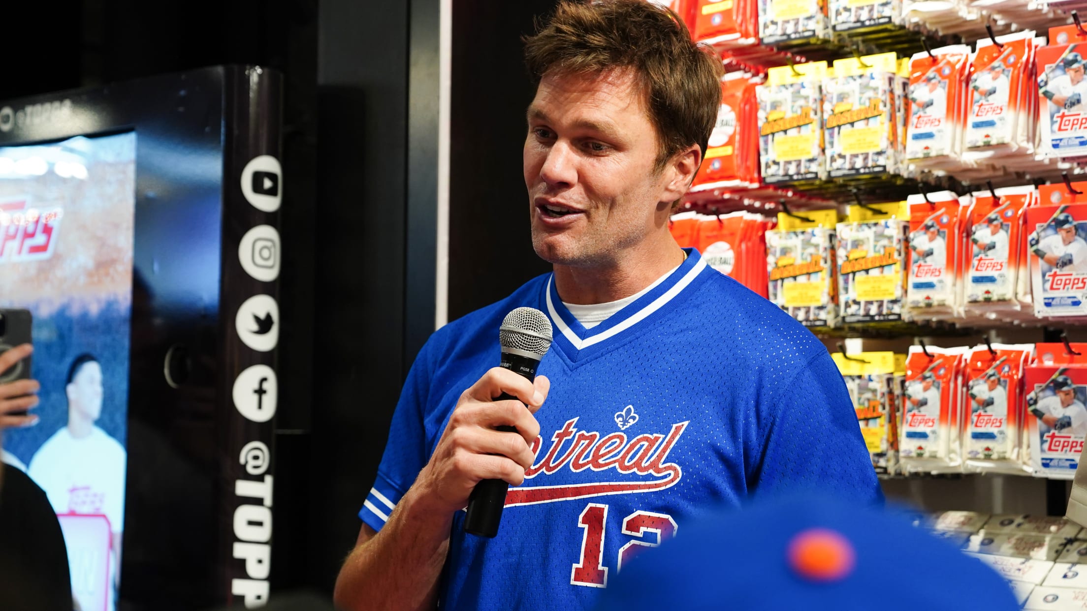 Tom Brady holds a microphone while wearing a Montreal Expos jersey