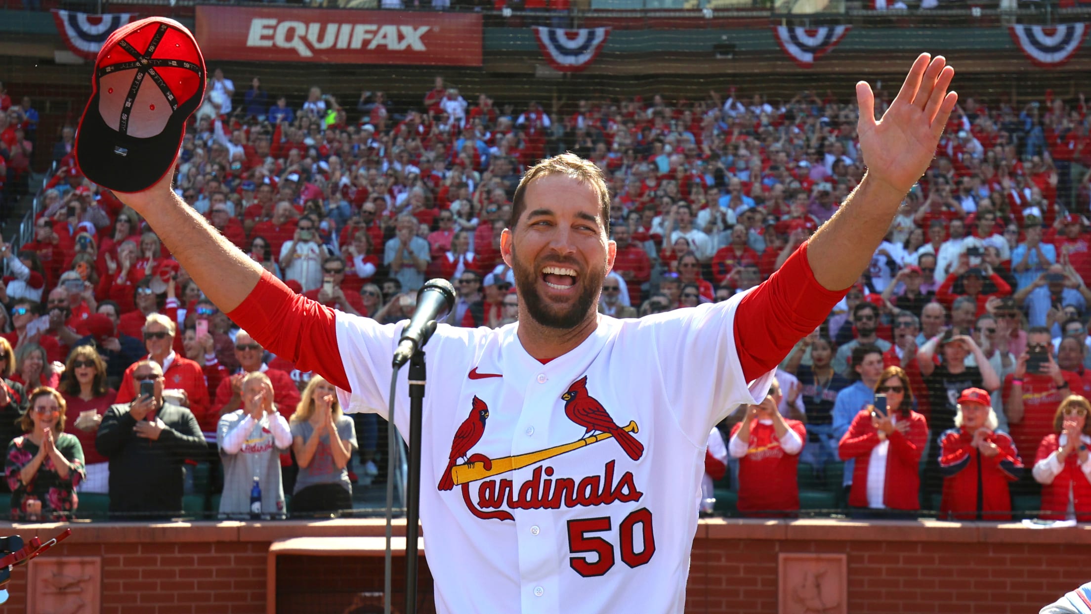 Adam Wainwright stands in front of a microphone, spreading his arms wide in appreciation