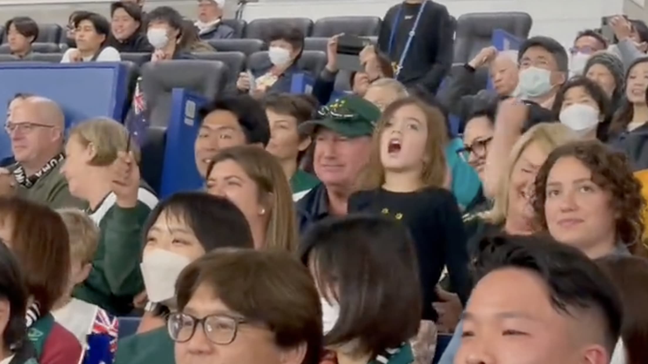 A screenshot of a girl standing in a crowd, cheering