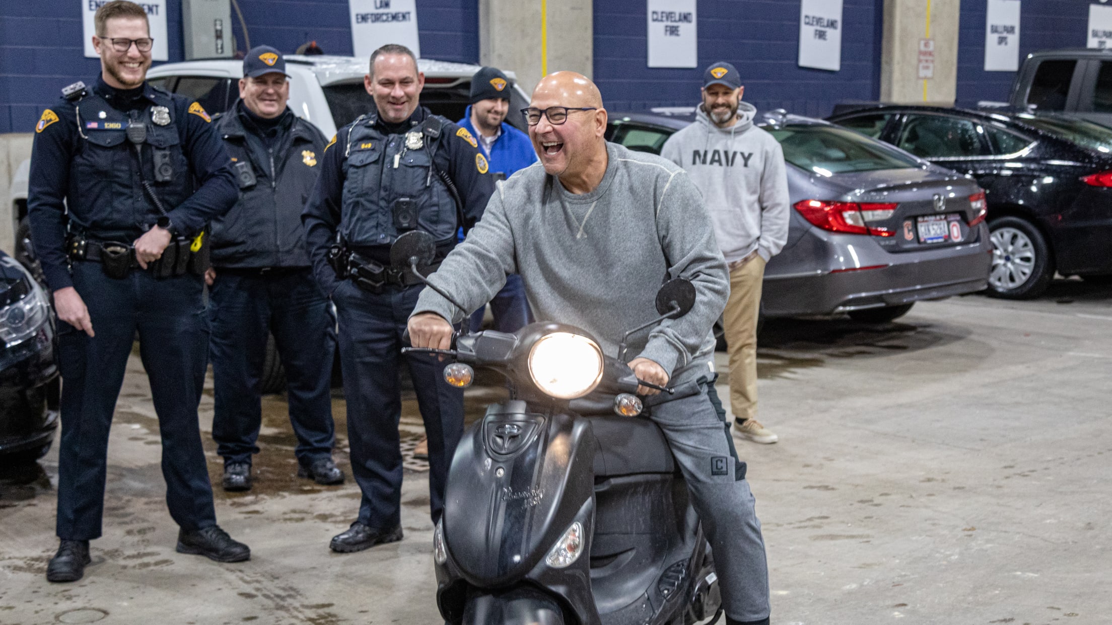 Guardians manager, in a gray sweatshirt, laughs as he sits on his scooter while police and others look on