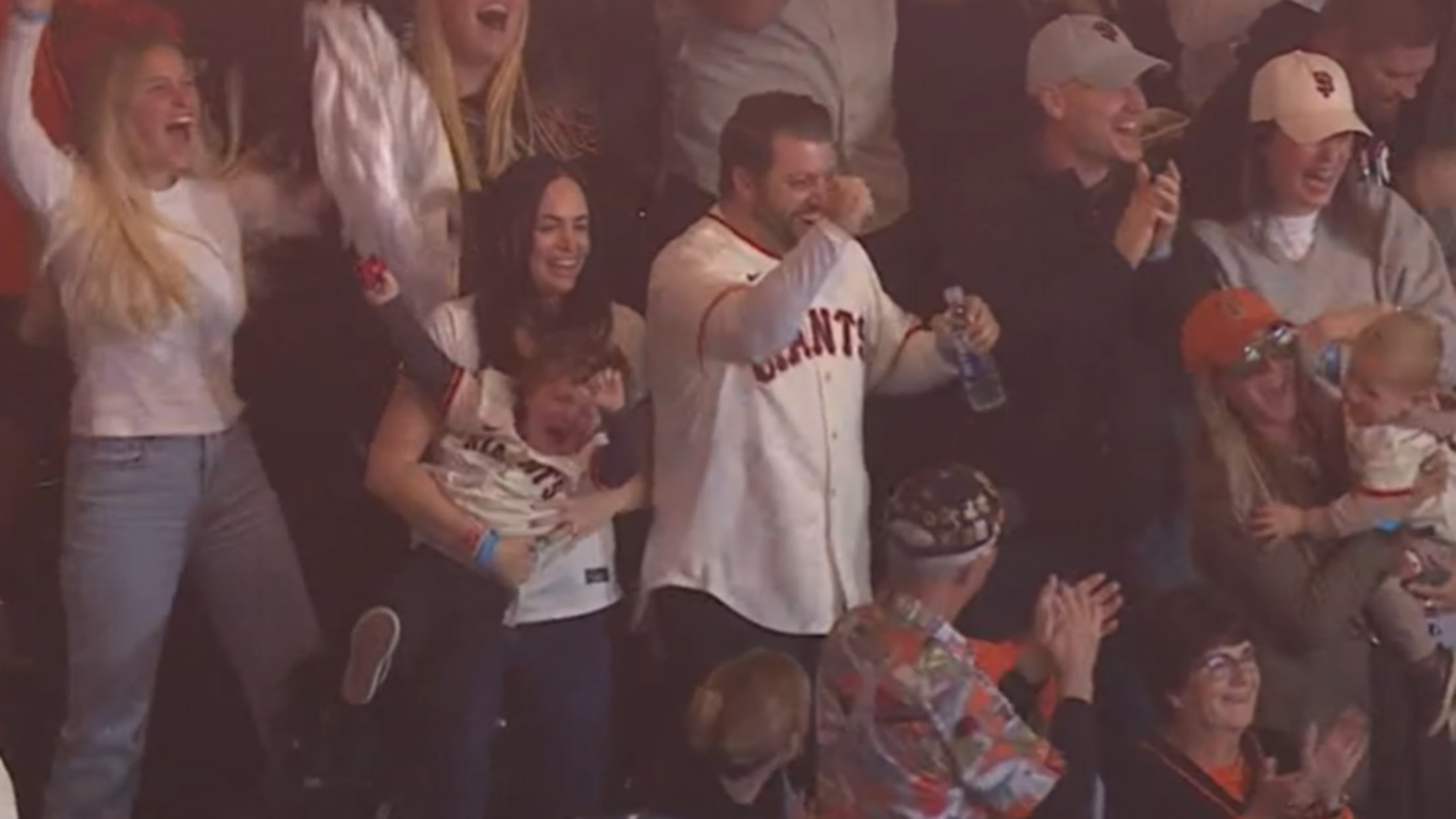 A woman smiles and holds a squirming child as Giants fans around her cheer