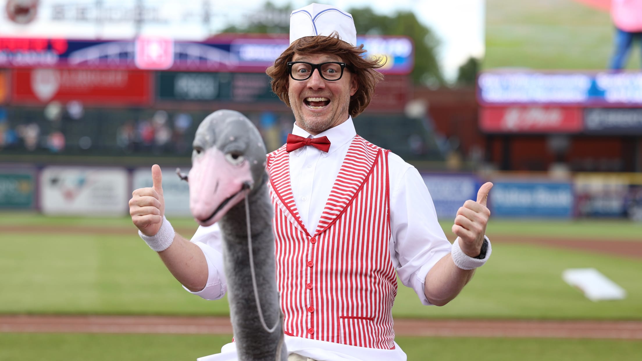 Matt Jackson gives two thumbs up in his vendor outfit featuring a red bowtie, red-and-white striped vest, a white hat, glasses and an ostrich