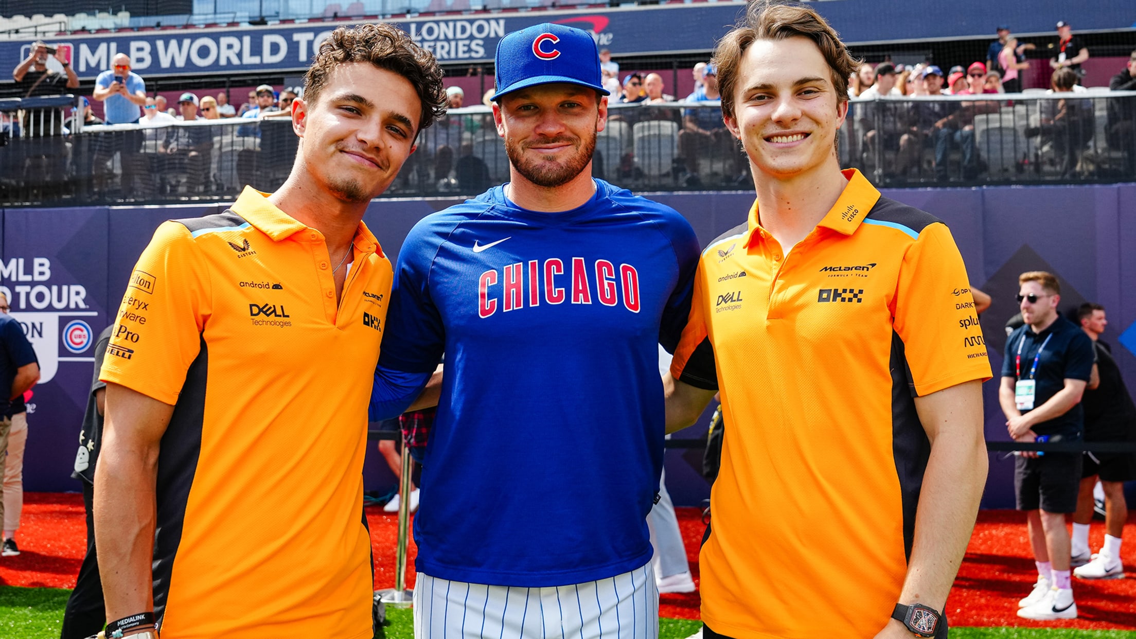 Ian Happ of the Cubs is flanked by Formula 1 drivers Oscar Piastri and Lando Norris