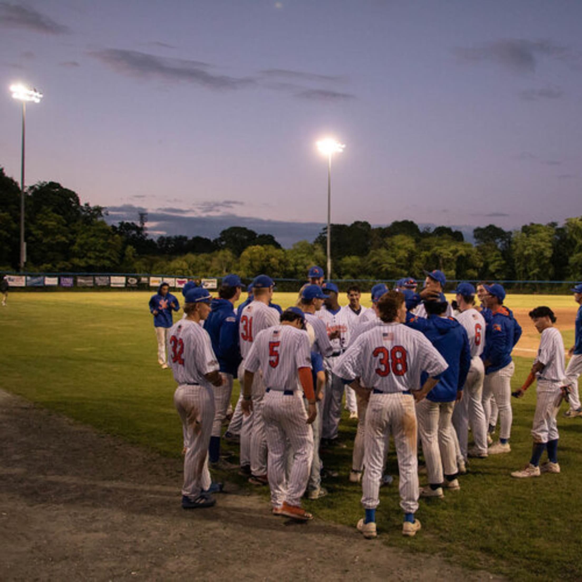 Hyannis players get into a large group on the field as the sun sets over Massachusetts.